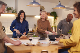 Group Of Mature Friends Meeting At Home Serving Food At Dinner Party And Drinking Wine Together